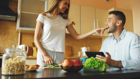 🎬 FULL 4K VIDEO for this still is in my bio link! ⬇️ Attractive couple chatting in the kitchen early morning. Beautiful woman feed her husband while cooking breakfast at home